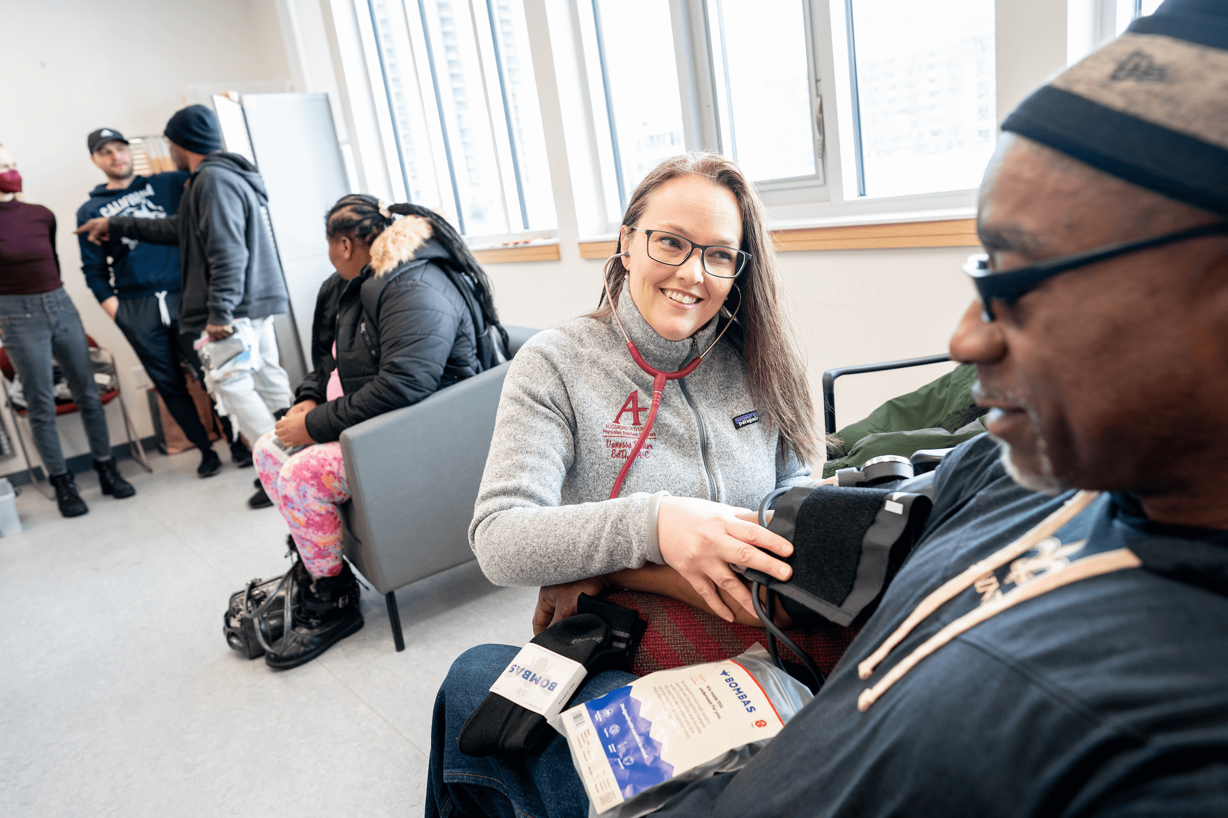 vanessa performing a blood pressure check on a member of the central lutheran health commons. people are standing and chatting in the background